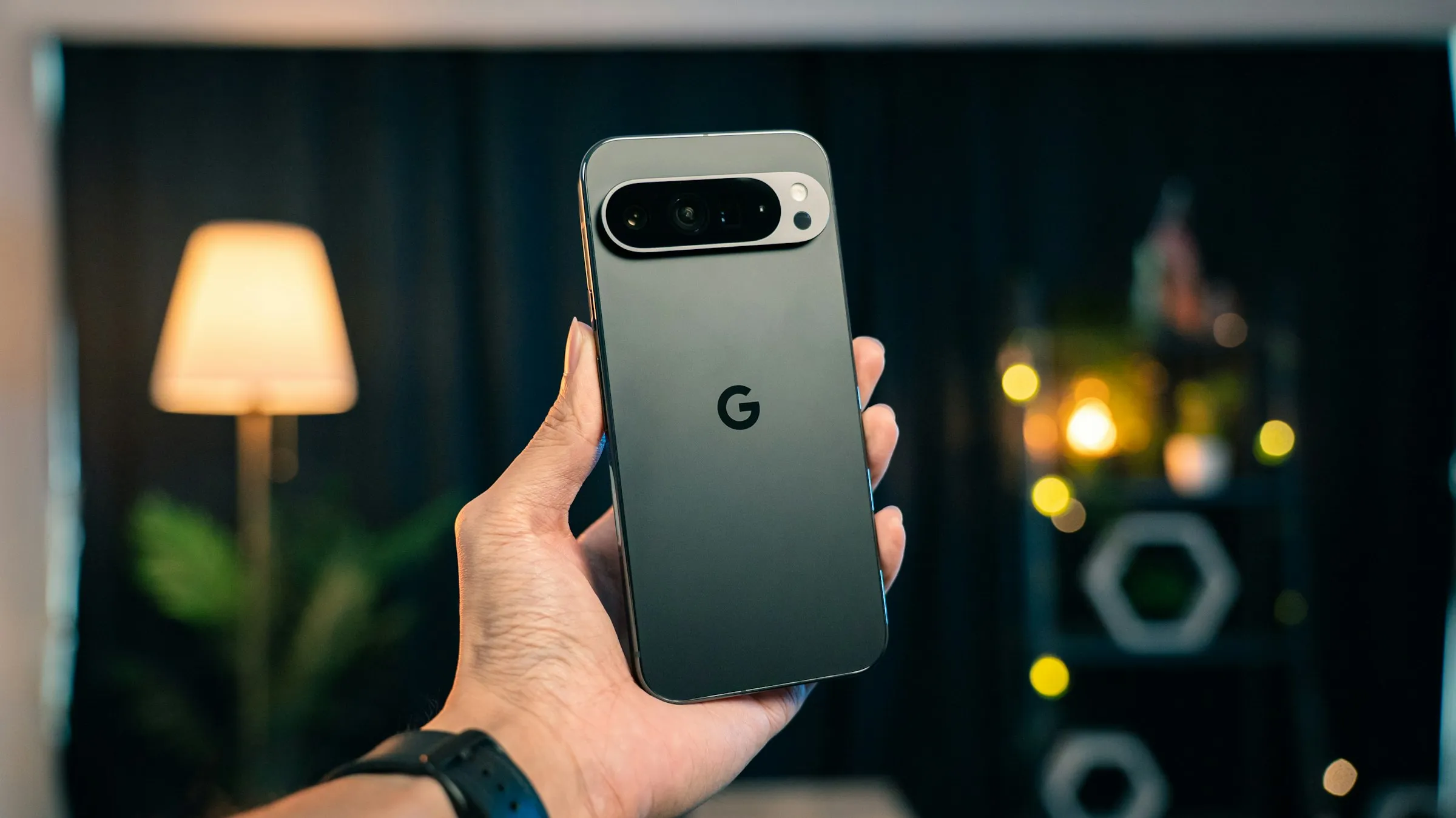 A hand holding up a Google Pixel phone, seen from the back, in a dimly lit room