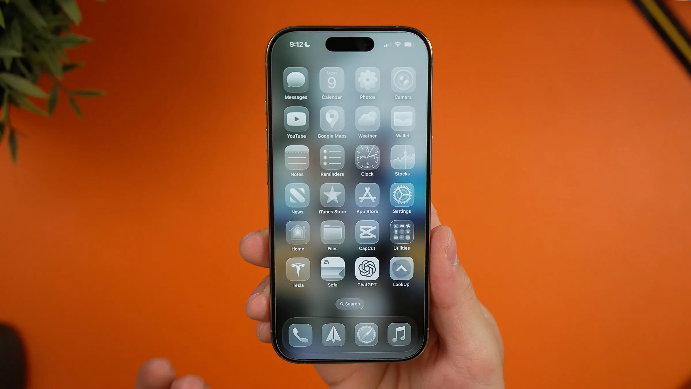 A hand holding an iPhone showing its home screen of app icons, against an orange wall
