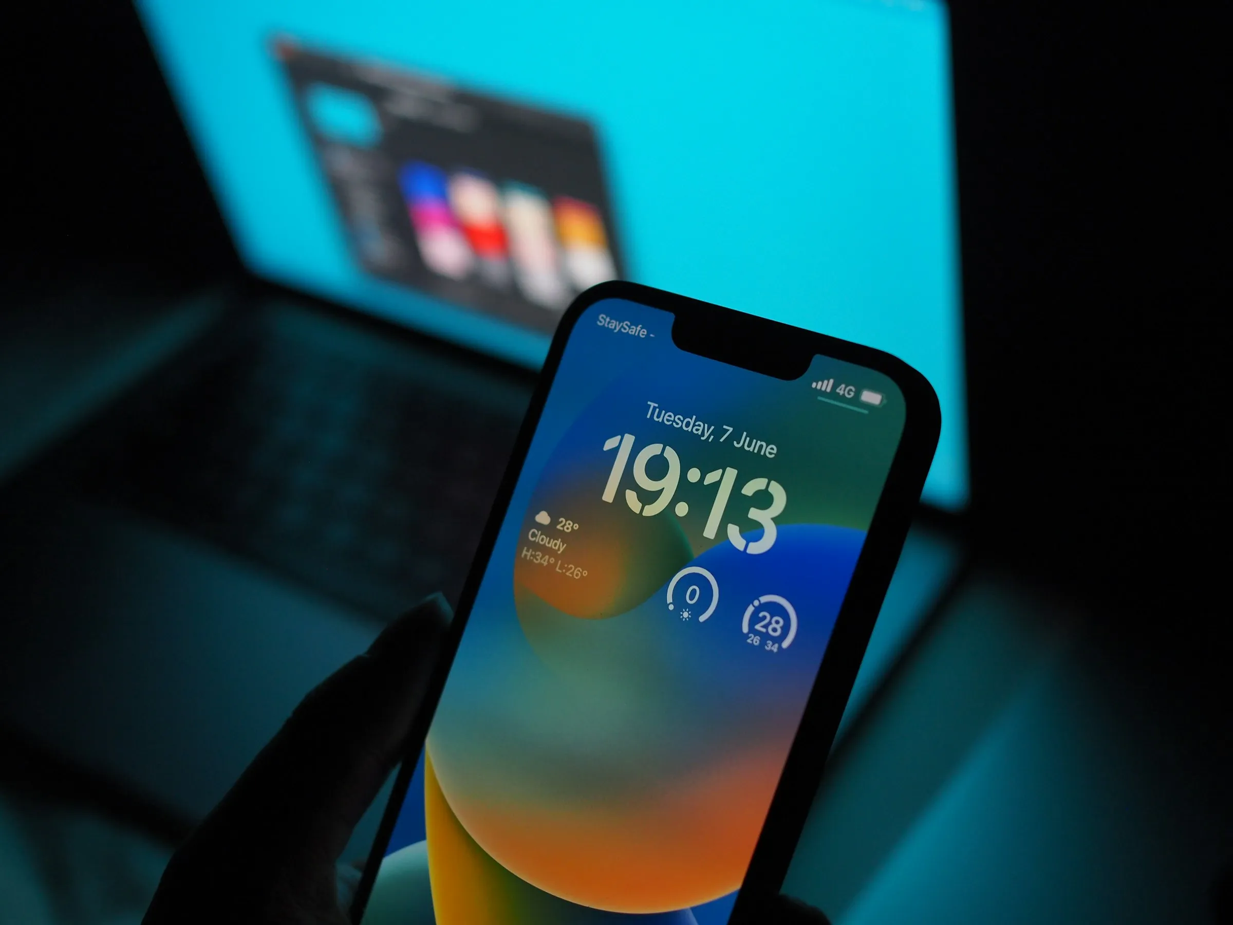 A hand holding an iPhone in front of a laptop screen, lit in blue